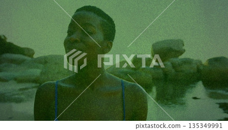 Wading woman standing in rocky shore tide pools, with thin-strap blue top beside green boulders Wading woman standing in rocky shore tide pools, with thin-strap blue top beside green boulders 135349991