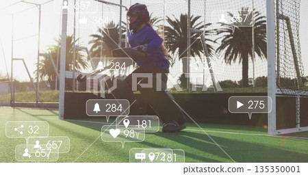 Kneeling teenage goalkeeper holding hockey stick wearing helmet on hockey turf, with social icons 135350001