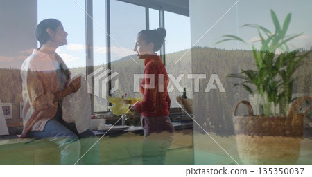 Mother and daughter chatting while holding mug and washing dishes wearing yellow gloves in kitchen 135350037