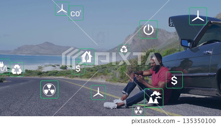 Checking man wearing red T-shirt holding smartphone on coastal road, open car hood, copy space 135350100