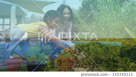 Kneeling mother and daughter planting seedlings on deck by modern house, with planter boxes 135350113