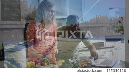Chopping vegetables on wooden cutting board, couple preparing salad at kitchen island with laptop Chopping vegetables on wooden cutting board, couple preparing salad at kitchen island with laptop 135350118