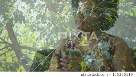 Gazing woman holding ceramic mug wearing floral top, eyeglasses by cafe window, foliage reflection Gazing woman holding ceramic mug wearing floral top, eyeglasses by cafe window, foliage reflection 135350119