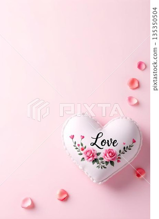 White heart pillow with delicate floral arrangement and 'Love' text on pink background with rose petals creating minimalist composition. Romantic design concept. 135350504