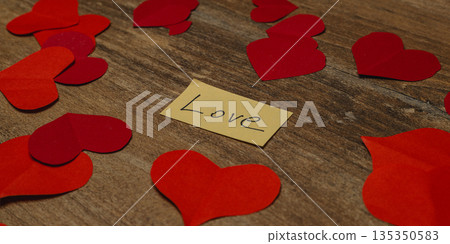 Hearts and message of love on a wooden table surrounded by paper cutouts Hearts and message of love on a wooden table surrounded by paper cutouts 135350583