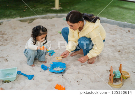 mother and child girl playing sand with toy on playground 135350614