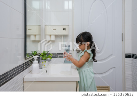 child girl washing her hands with soap in bathroom sink for hygiene child girl washing her hands with soap in bathroom sink for hygiene 135350632