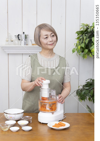 一位老年婦女在廚房裡用食物料理機做飯。 135350665