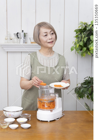 一位老年婦女在廚房裡用食物料理機做飯。 135350669