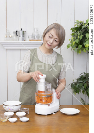 一位老年婦女在廚房裡用食物料理機做飯。 135350673