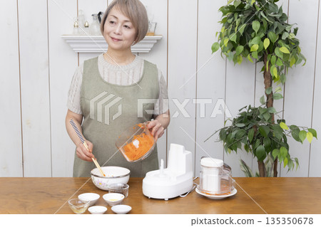 一位老年婦女在廚房裡用食物料理機做飯。 135350678