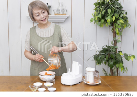 一位老年婦女在廚房裡用食物料理機做飯。 135350683