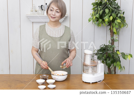 一位老年婦女在廚房裡用食物料理機做飯。 135350687
