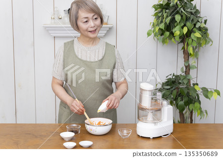 一位老年婦女在廚房裡用食物料理機做飯。 135350689
