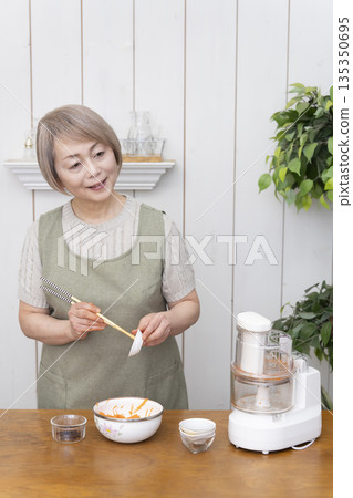 一位老年婦女在廚房裡用食物料理機做飯。 135350695