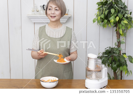 一位老年婦女在廚房裡用食物料理機做飯。 135350705