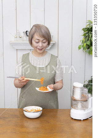 一位老年婦女在廚房裡用食物料理機做飯。 135350710
