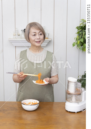 一位老年婦女在廚房裡用食物料理機做飯。 135350711