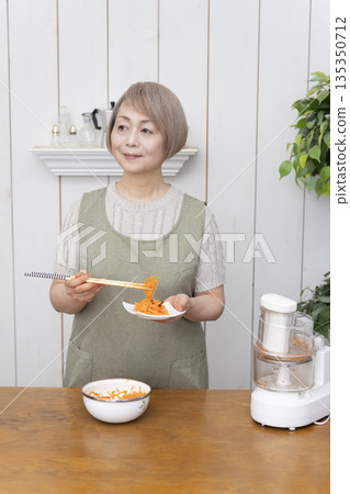 一位老年婦女在廚房裡用食物料理機做飯。 135350712