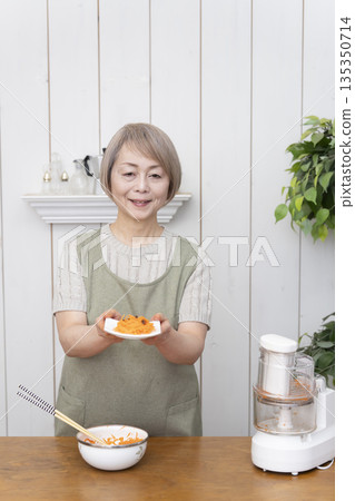 一位老年婦女在廚房裡用食物料理機做飯。 135350714