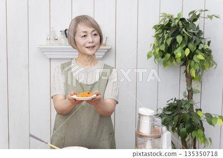 一位老年婦女在廚房裡用食物料理機做飯。 135350718