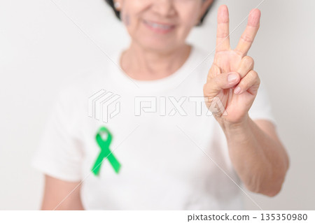 Elderly with Green Ribbon for concept of March world Bipolar disorder day, Cerebral Palsy Awareness month, kidney disease Cancer and Traumatic Brain Injury, TBI. Healthcare and world cancer day 135350980