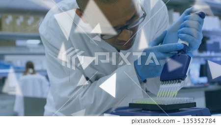 Dispensing technician wearing safety glasses, lab coat using pipette into microplate at lab bench 135352784