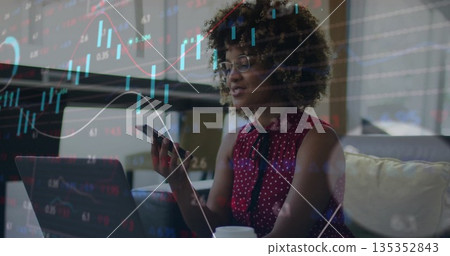 Woman wearing red blouse analyzing charts on laptop in living room, smartphone, coffee cup 135352843