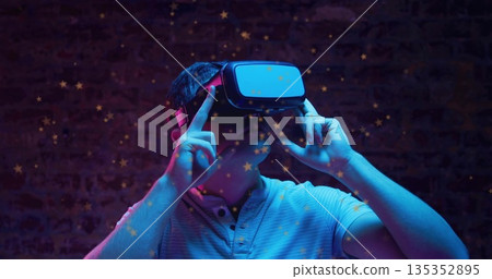 Man wearing light polo shirt adjusting virtual reality headset in studio, with star overlays Man wearing light polo shirt adjusting virtual reality headset in studio, with star overlays 135352895