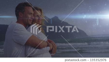 Embracing middle-aged couple wearing white shirts watching dusk sky at beach with waves, copy space Embracing middle-aged couple wearing white shirts watching dusk sky at beach with waves, copy space 135352976