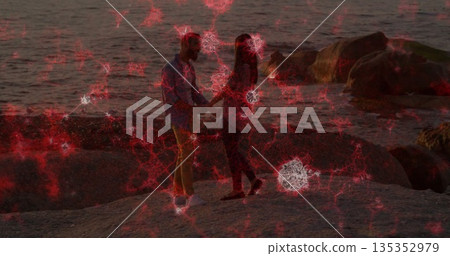 Holding hands couple standing facing rocky shoreline at dusk, with red white network overlay Holding hands couple standing facing rocky shoreline at dusk, with red white network overlay 135352979