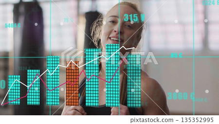 Smiling woman wearing black top and boxing gloves in gym, with punching bags, windows and overlay 135352995