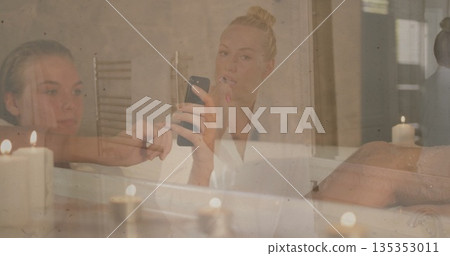 Brushing teeth bathrobe woman holding toothbrush as friend checking smartphone at bathroom mirror Brushing teeth bathrobe woman holding toothbrush as friend checking smartphone at bathroom mirror 135353011