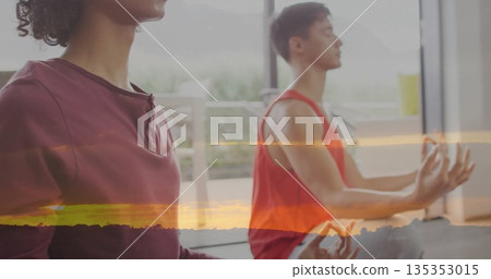Friends wearing yogawear meditating crosslegged on mats in sunrise studio, with windows and plants Friends wearing yogawear meditating crosslegged on mats in sunrise studio, with windows and plants 135353015