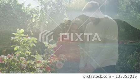 Couple strolling in sunny garden, with roses, trees and glass reflecting mountain and lake view 135353019