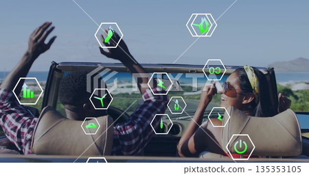 Cruising interracial couple in convertible waving arms on coastal road, with eco icons 135353105