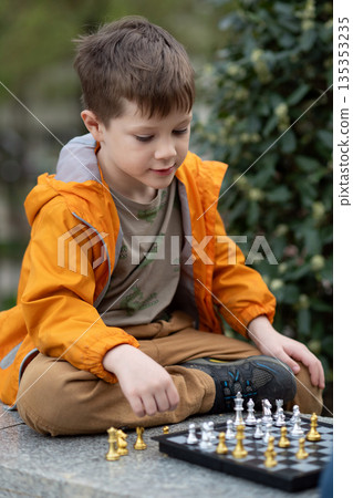 Boy playing chess outdoor. Learning strategic game. Education. 135353235