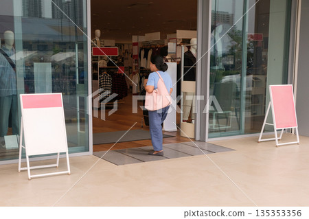 Woman enters store with shopping bags and looks around in busy retail area during daytime Woman enters store with shopping bags and looks around in busy retail area during daytime 135353356