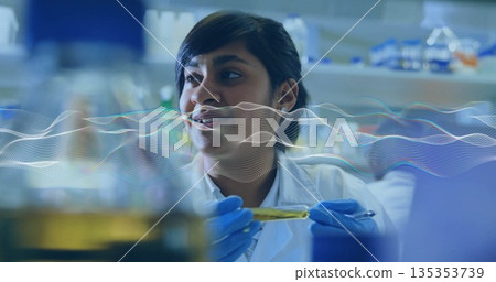 Examining scientist wearing lab coat holding yellow test tube at lab bench, with pipette 135353739