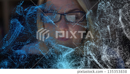Woman wearing rectangular eyeglasses analyzing particles in dim lab, with holographic display 135353838