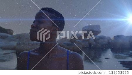 Standing woman closing eyes in water at rocky shoreline, with blue swimsuit and granite boulders 135353955