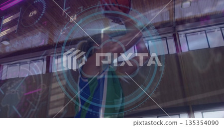 Female athlete holding basketball overhead in sports hall, with digital overlay and jersey Female athlete holding basketball overhead in sports hall, with digital overlay and jersey 135354090