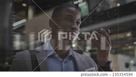 Speaking businessman recording voice message on smartphone in office lobby, with analytics overlay Speaking businessman recording voice message on smartphone in office lobby, with analytics overlay 135354594