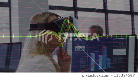 Woman wearing blazer and VR headset analyzing data using dual monitors at office desk, copy space 135354597