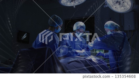 Performing surgery surgical team wearing gowns operating in OR, with lights and surgical table 135354608