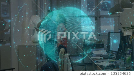 Projecting digital holographic globe overlaying modern office desks, with monitors, mugs and plants 135354625