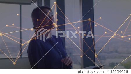 Standing woman wearing blue blazer near office window, holding tablet with digital network overlay Standing woman wearing blue blazer near office window, holding tablet with digital network overlay 135354626