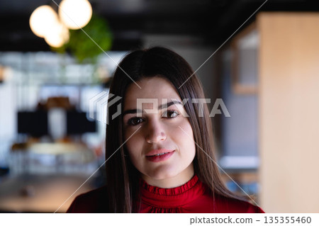 Woman working in open-plan office wearing red blouse among desks computer monitors and plant Woman working in open-plan office wearing red blouse among desks computer monitors and plant 135355460