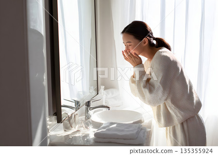 一位日本女性正在鏡子前檢查皮膚。圖片展示了護膚和美容流程。 135355924