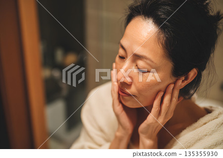 一位日本女性正在鏡子前檢查皮膚。圖片展示了護膚和美容流程。 135355930
